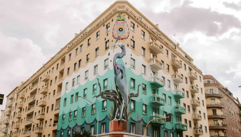 Un maestoso airone blu e tentacoli di polpo adornano un palazzo nel quartiere Ostiense, un'opera d'arte urbana che cattura lo sguardo.