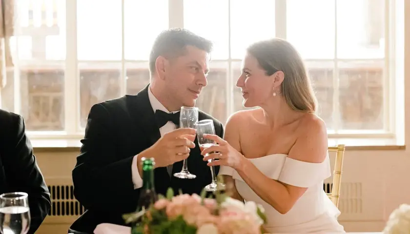 Para młoda wznosi toast kieliszkami szampana. W tle okna, idealne na romantyczne piosenki na wesele.