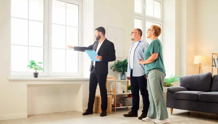 Agente inmobiliario explica a pareja cuánto dura una tasación, señalando la luz natural de la vivienda.