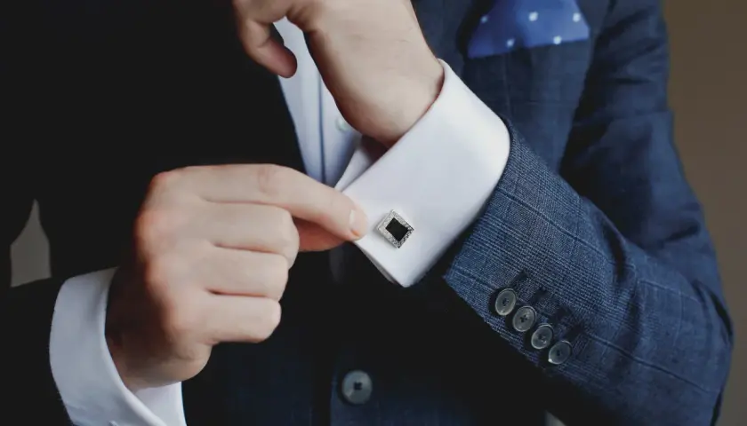 Mann schließt Manschettenknöpfe an seinem Hemd. Was ist eine Manschette? Ein elegantes Accessoire, das den Hemdsärmel verschließt und Stil verleiht.