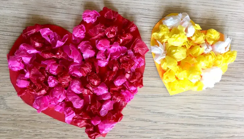 Zwei bunte Herzen, rot und gelb, mit zerknülltem Seidenpapier beklebt. Ein schönes Beispiel für herz basteln kinder.