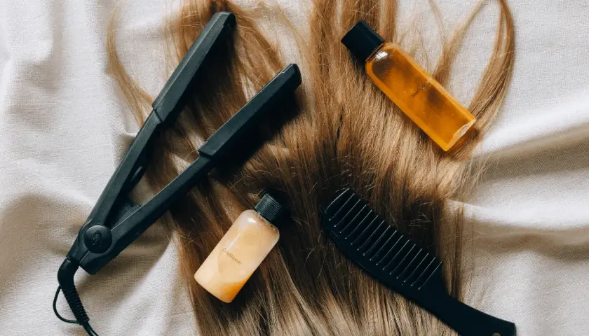 Plancha, peine y botellitas de champú y acondicionador sobre cabello rubio. Una solución casera para el pelo naranja.