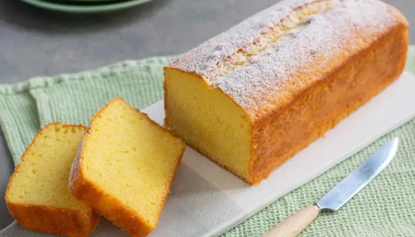 Un soffice plumcake yogurt, spolverato di zucchero a velo, pronto per essere gustato. Due fette sono già state tagliate.