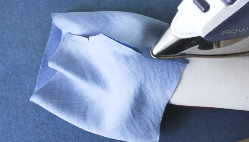 Ironing a folded cuff band to a light blue sleeve. This step is crucial for how to sew a folded cuff band to a sleeve.