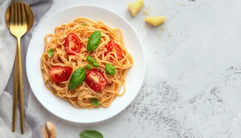 Leckere Tagliatelle Rezepte: Spaghetti mit Tomaten, Basilikum und Parmesan auf einem Teller, daneben goldene Gabel und Messer.