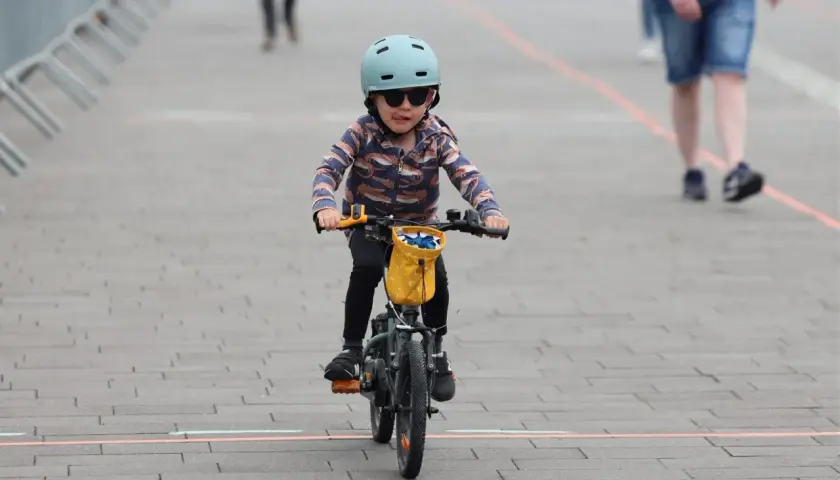 Małe dziecko w kasku i okularach przeciwsłonecznych śmiga na rowerze, wyciągając język. To dziecko na rowerze przepisy, jak prawdziwy mistrz.