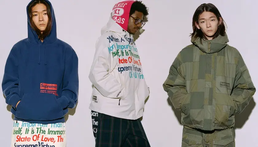 Trzech mężczyzn w ubraniach z kolekcji Junya Watanabe x Supreme. Jeden w granatowej bluzie, drugi w białej kurtce z tekstem, trzeci w zielonej, patchworkowej kurtce.
