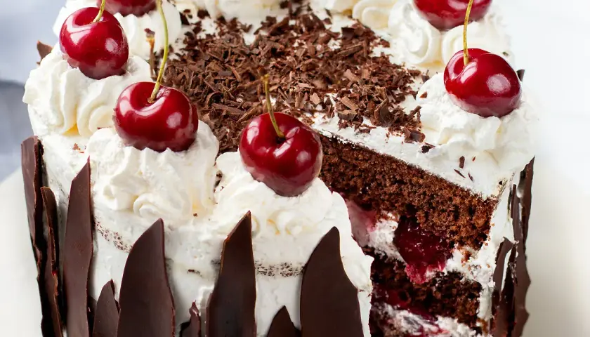 Una fetta di foresta nera torta, con panna montata, ciliegie e scaglie di cioccolato.