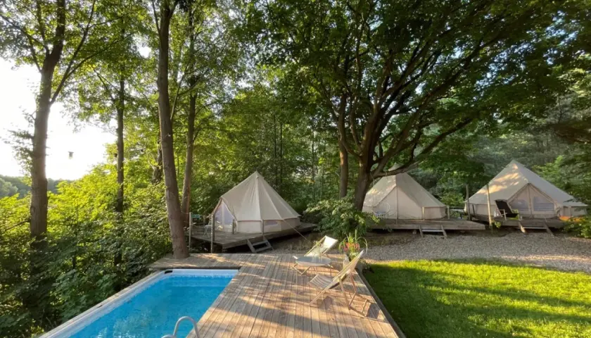 Luksusowy glamping nad jeziorem: namioty tipi na drewnianych tarasach, basen i leżaki wśród drzew. Idealne miejsce na relaks.