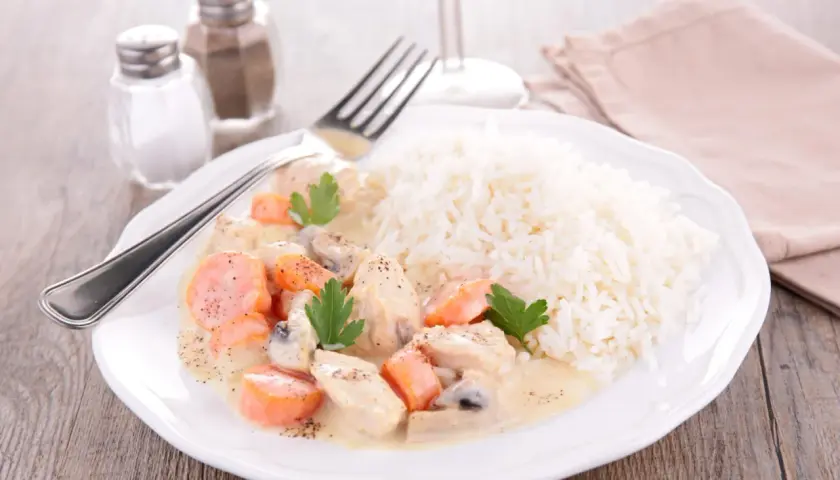 Une assiette de blanquette de veau crémeuse avec des carottes et des champignons, servie avec du riz blanc. Un verre de vin de Bordeaux est suggéré pour accompagner ce plat.