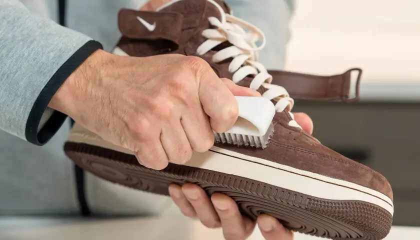 Man limpiando serraje de una zapatilla marrón con un cepillo blanco.