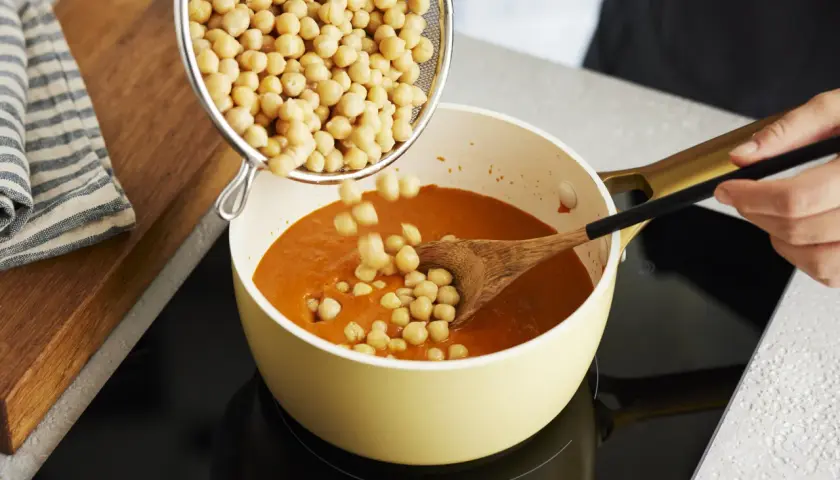 Kichererbsen werden in einen Topf mit Curry gegeben. Perfekt für die Zubereitung von Kichererbsen-Curry zum Einfrieren.