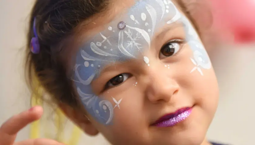 Bambina con trucco da fata del ghiaccio per il carnevale, con glitter viola sulle labbra e disegni bianchi e azzurri sul viso.