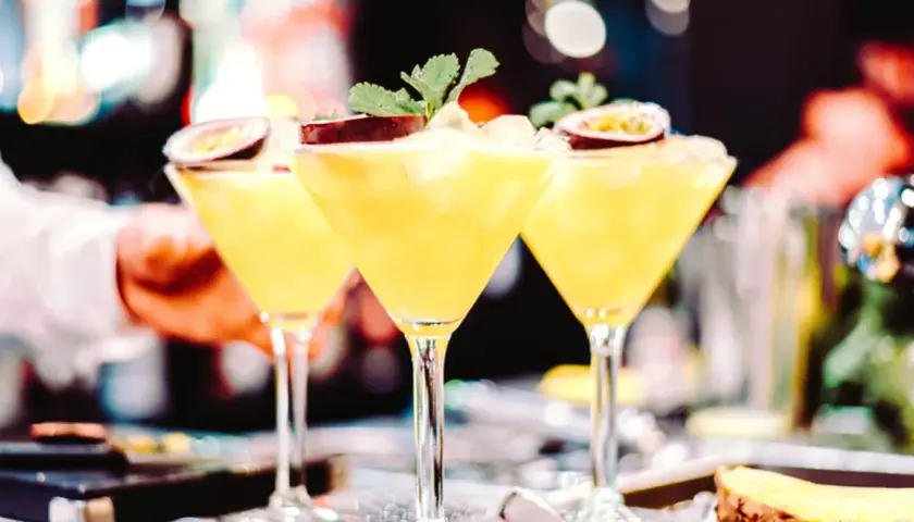 Trzy kieliszki z orzeźwiającą mango margarita, ozdobione połówkami marakui i listkami mięty, gotowe do podania.