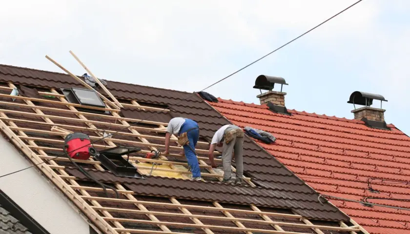 Deux couvreurs travaillent sur une toiture en cours de rénovation, préparant à prolonger un toit existant.