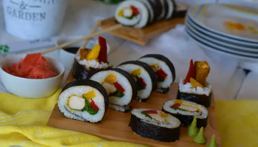 Pyszne sushi z kurczakiem, papryką i mango na desce. Obok miseczka z imbirem i sos sojowy.