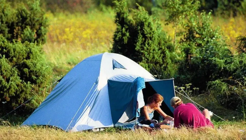 Para spędza czas w namiocie, idealne miejsce na biwak. Otoczeni zielenią i polnymi kwiatami, cieszą się spokojem natury.