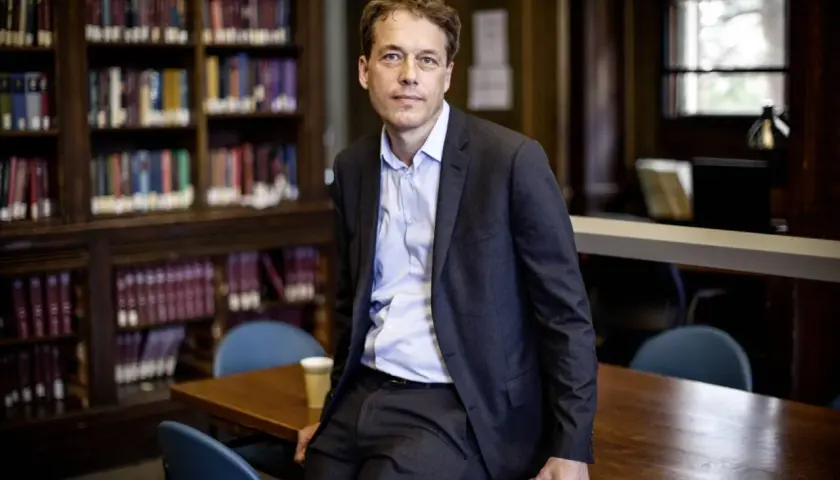 Sven Beckert sitzt in einer Bibliothek, umgeben von Büchern.