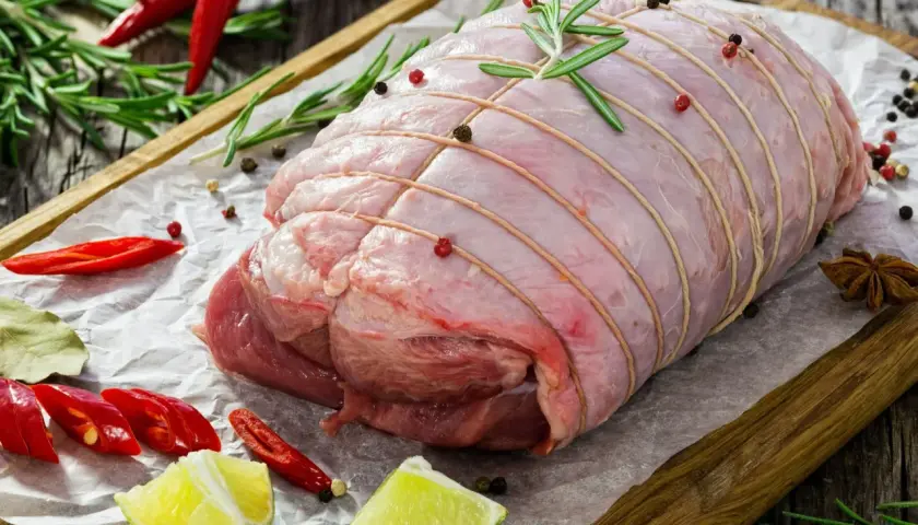Surowa rolada z indyka, związana sznurkiem, z dodatkiem rozmarynu, pieprzu, chili i limonki, czeka na pieczenie.