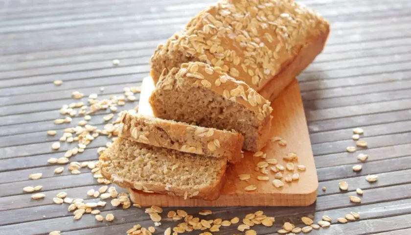 Pane proteico integrale, cosparso di fiocchi d'avena, affettato su un tagliere di legno.