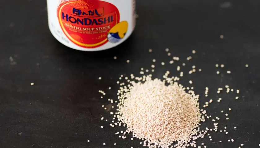 A jar of Hondashi soup stock sits next to a pile of granules. This image helps visualize the dashi powder to water ratio for perfect Japanese broth.