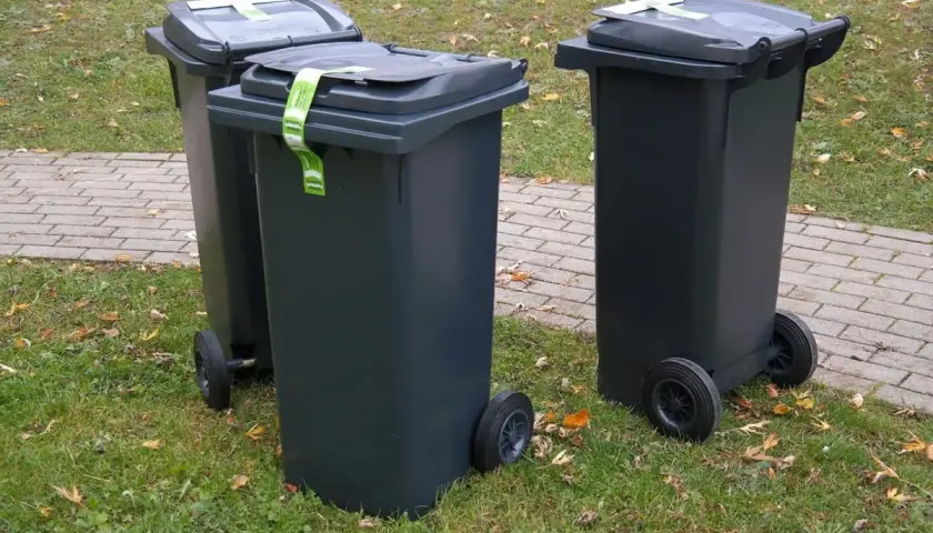 Trzy szare kosze na śmieci stoją na trawie. Zastanawiasz się, gdzie wyrzucić kołdrę z pierza? Sprawdź lokalne przepisy dotyczące odpadów wielkogabarytowych.