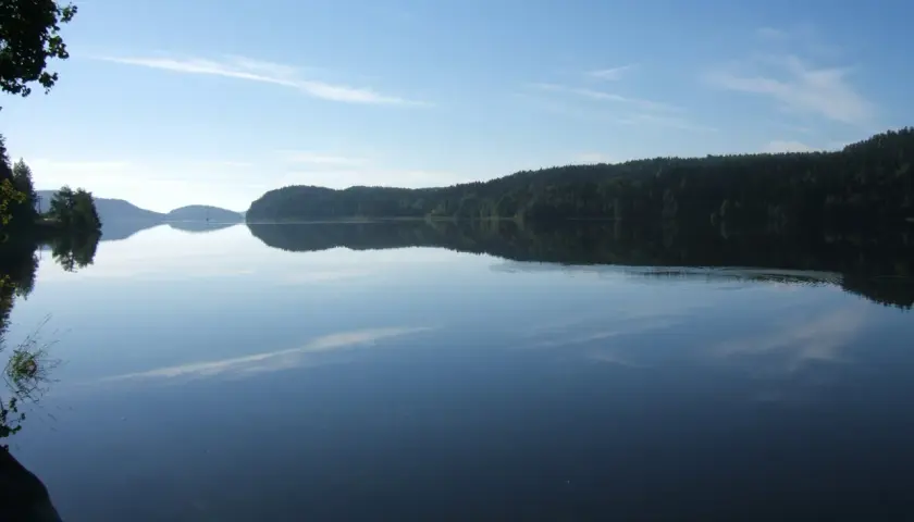 Calmo lago riflette la foresta e il cielo azzurro. Chissà se è il lago più grande d'Europa, con questa pace.