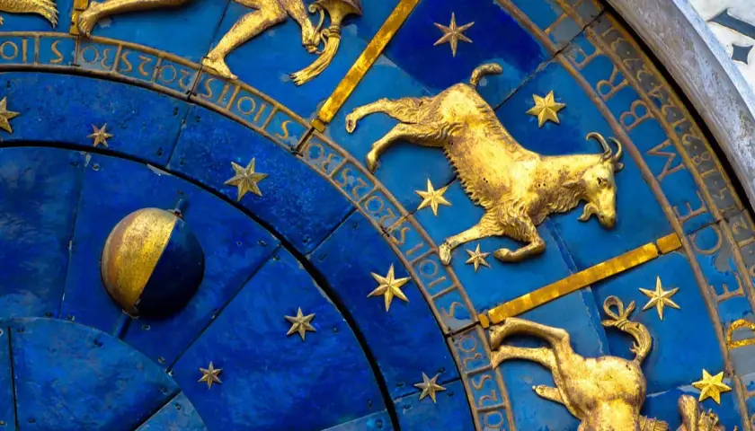 Złote figury Koziorożca i innych znaków zodiaku na niebieskiej tarczy zegara. 19 stycznia to czas Koziorożca.