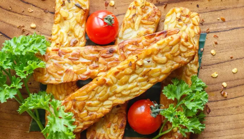 Złociste kawałki tempeh, smażone na złoto, z pomidorkami i natką pietruszki. Tempeh co to? To pyszna, roślinna alternatywa!
