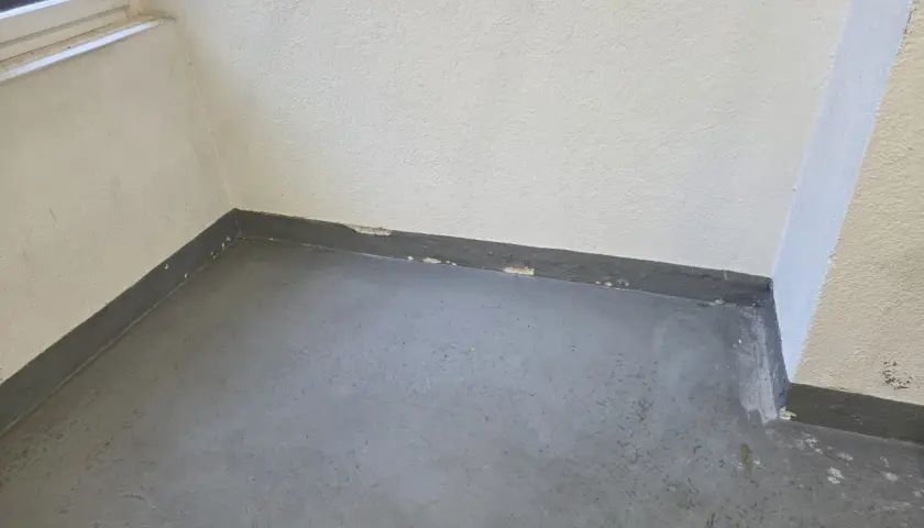 Ecke eines Raumes mit grauem Boden und weißer Wand. Der graue Sockelbereich zeigt Abplatzungen, ein Zeichen dafür, ab wann ist ein Keller feucht.
