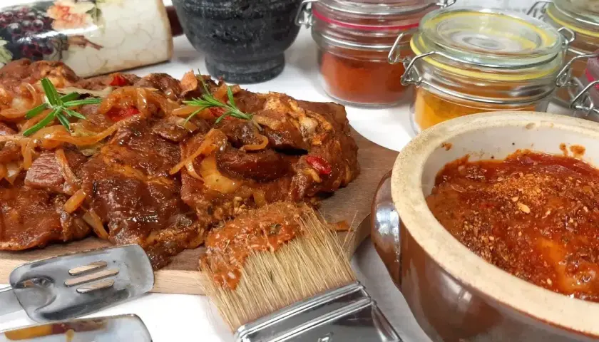 Karkówka na grilla w aromatycznej marynacie, gotowa do pieczenia. Obok pędzel z marynatą, przyprawy i narzędzia.