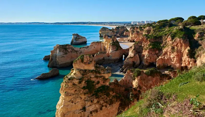 Acantilados dorados y mar turquesa en las **playas de Portugal**. Un paisaje idílico con formaciones rocosas y vegetación exuberante.