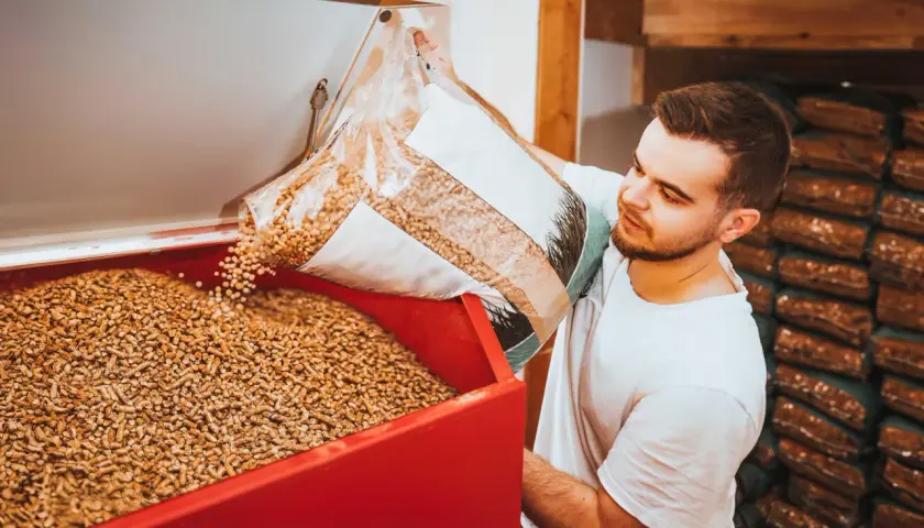 Mann füllt Holzpellets in einen Behälter. Die Pellets preisentwicklung ist ein wichtiges Thema für Heizungsbesitzer.