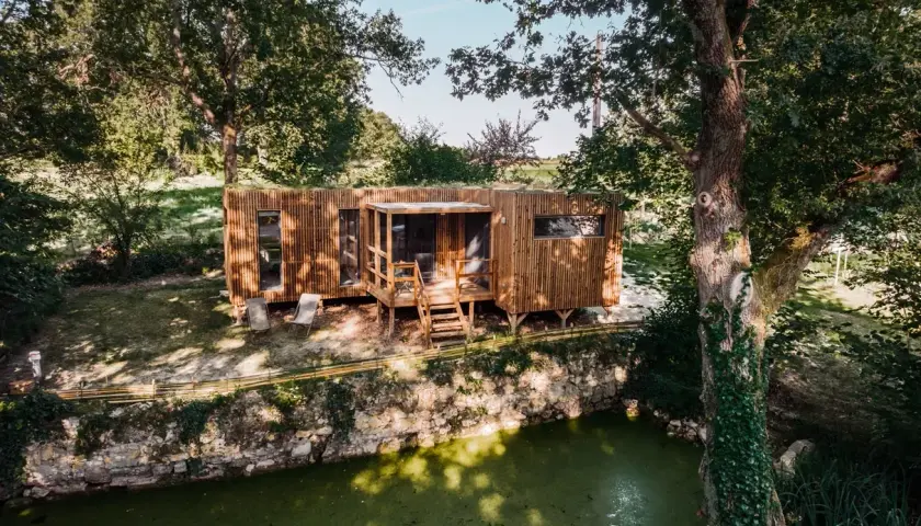 Une maison bioclimatique en bois, perchée près d'un étang verdoyant, entourée d'arbres majestueux.