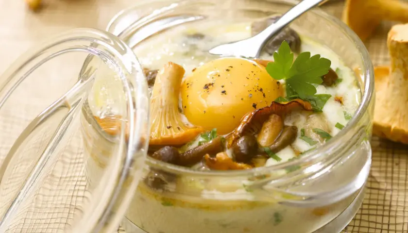 Un œuf au plat, entouré de champignons et de persil, dans un ramequin en verre. Un plat savoureux d'œufs au four.