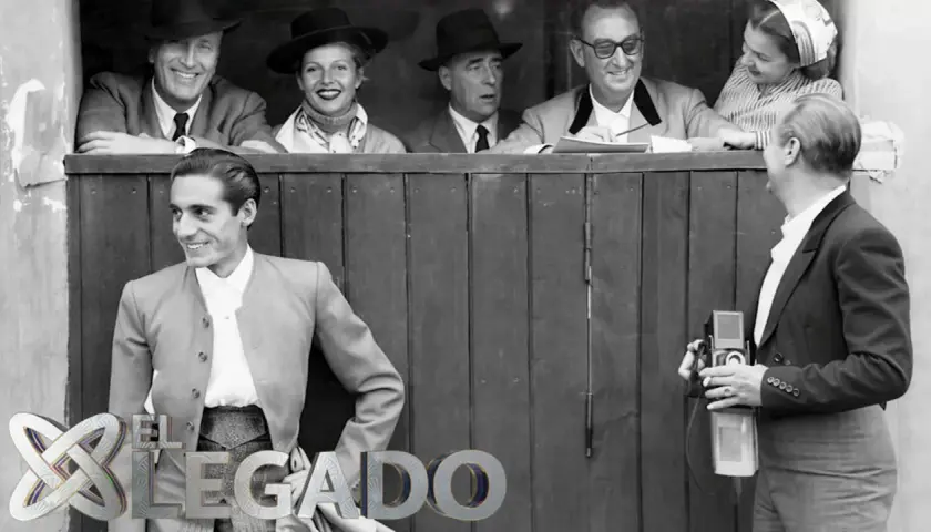 Un torero posa sonriente, mientras un fotógrafo captura el momento. Detrás, un grupo de espectadores, evocando la época de los toreros de los 90.