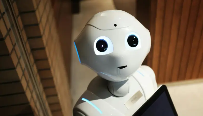 Der humanoide Roboter Pepper mit leuchtenden Augen und blauen Akzenten hält ein Tablet. Er ist bereit für eine audio ki-gesteuerte Interaktion.