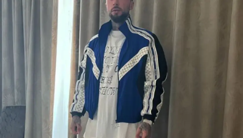 Malik Montana w niebieskiej kurtce i białej koszulce, gotowy na spotkanie z malik montana dzieci.