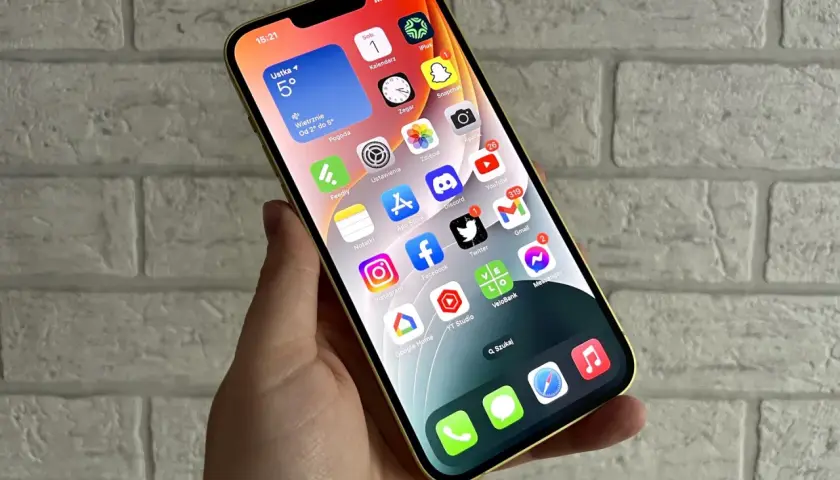 Złoty iPhone z widokiem na ekran główny, gdzie widać aplikacje takie jak pogoda, kalendarz, zdjęcia, YouTube, Gmail. Idealny do codziennej komunikacji i rozrywki, a także do wymiany informacji.