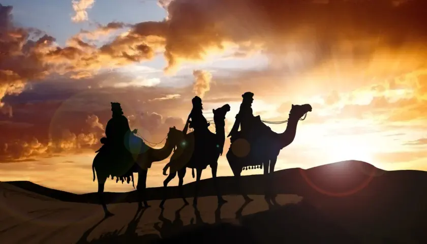 Drei Könige reiten auf Kamelen durch die Wüste bei Sonnenuntergang. Ein festlicher Anblick am 6. Januar.