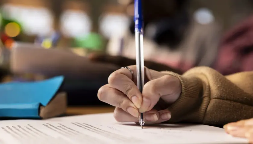Dłoń pisze długopisem na papierze, przygotowując serdeczne życzenia po angielsku.