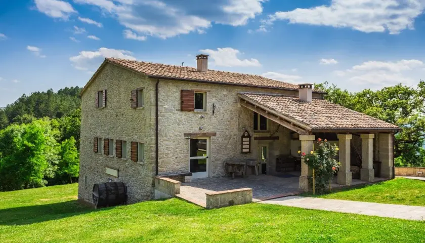Belle ferme en pierre, résultat d'une rénovation réussie, nichée dans un paysage verdoyant sous un ciel bleu.