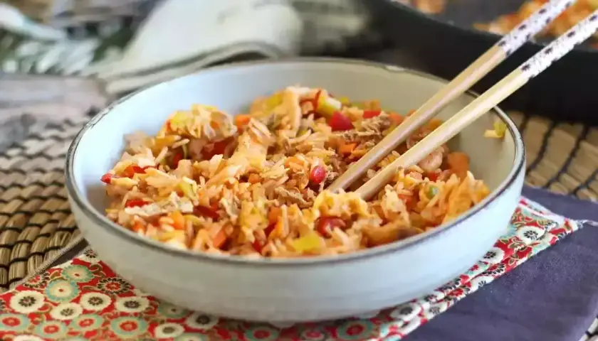 Miseczka pełna aromatycznego nasi goreng z warzywami i kawałkami kurczaka, gotowa do jedzenia pałeczkami.