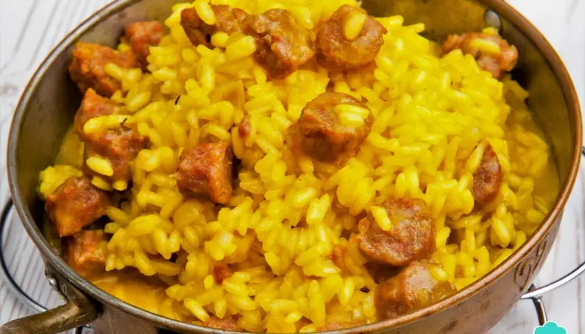 Arroz a la milanesa, un plato amarillo vibrante con trozos de salchicha, servido en un cuenco de cobre.
