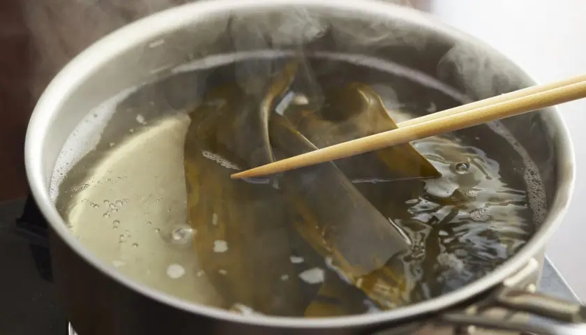 Kombu water steams in a pot as chopsticks gently hold the seaweed, infusing the broth with umami.