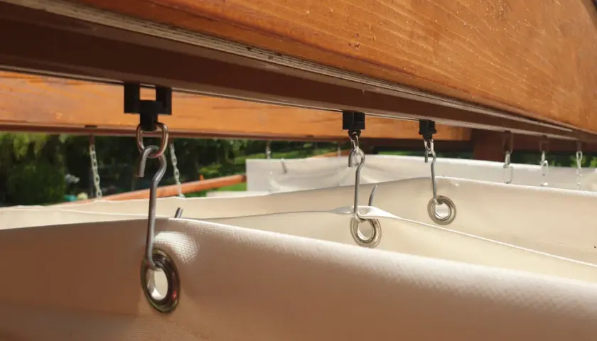 System mocowania rolety rzymskiej poziomej DIY. Metalowe haczyki łączą tkaninę z szyną pod drewnianą belką.
