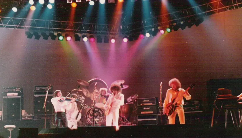 Zespół Electric Light Orchestra na scenie, grający największe przeboje. Kolorowe światła sceniczne podkreślają atmosferę koncertu.
