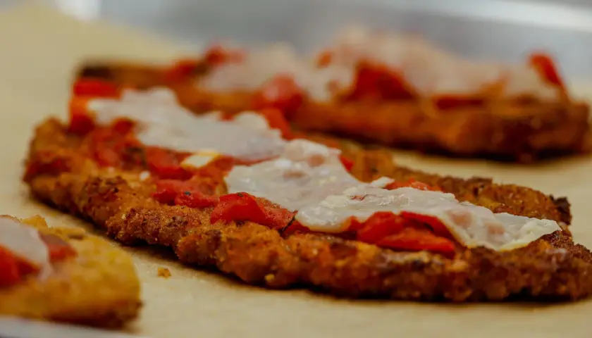 Escalopes de veau panées, garnies de sauce tomate et de mozzarella fondue, prêtes à être enfournées pour une délicieuse recette italienne parmigiana.