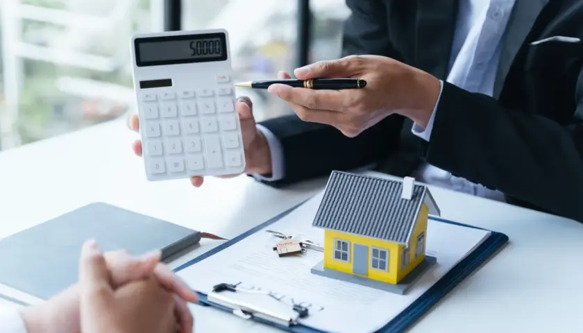 Conseiller montrant un calcul sur une calculatrice pour une aide premier achat immobilier. Une maison miniature et des clés sont sur un contrat.