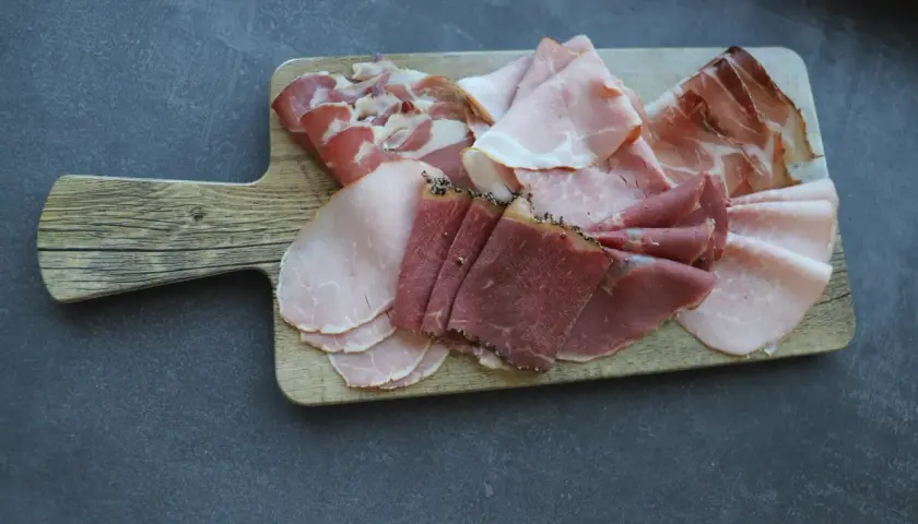 Holzbrett mit verschiedenen Aufschnittsorten, darunter zarter **prosciutto crudo**, Schinken und Rindfleisch.